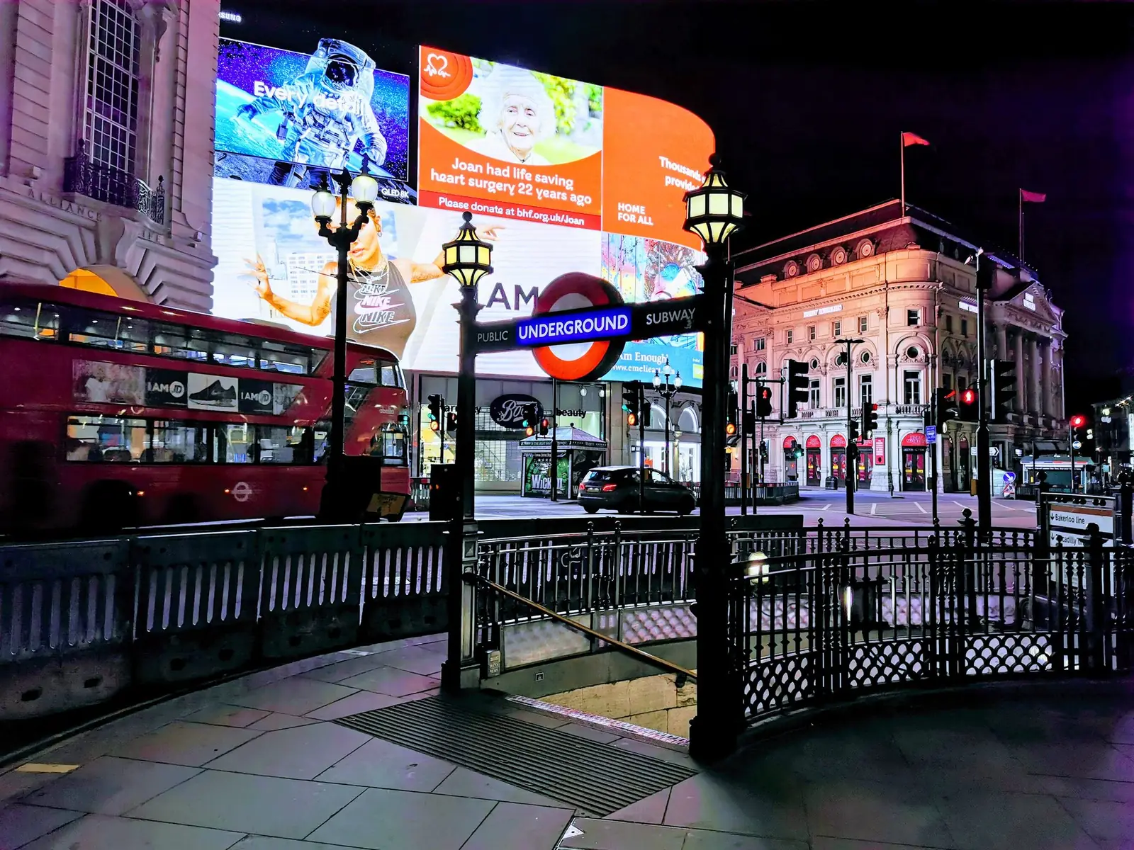 Hyrja e metrosë së Londrës te Piccadilly Circus natën, me tabelën e metrosë mbi shkallët dhe një autobus të kuq pas saj